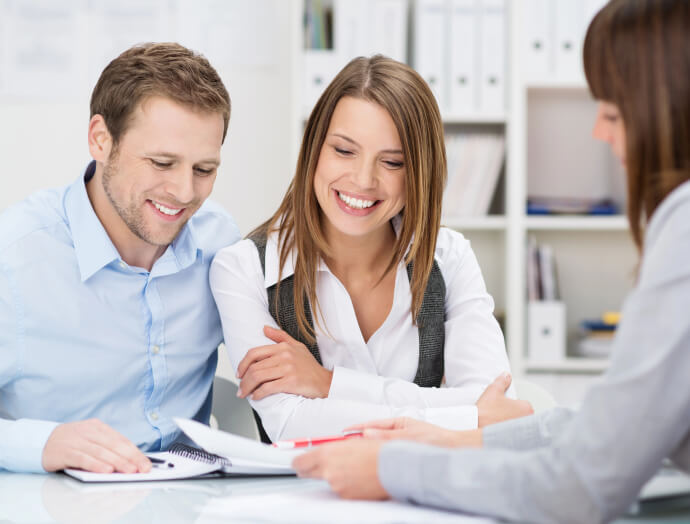 Traja ľudia na obchodnom stretnutí, dvaja s úsmevom, keď si prezerajú dokumenty Finmajster, sedia pri stole v kancelárskom prostredí.