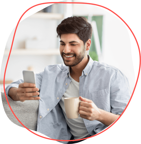 Muž usmievajúci sa na telefón, vychutnávajúci si moment Signálu, zatiaľ čo držal hrnček, pohodlne sedel na gauči v neformálnom prostredí.