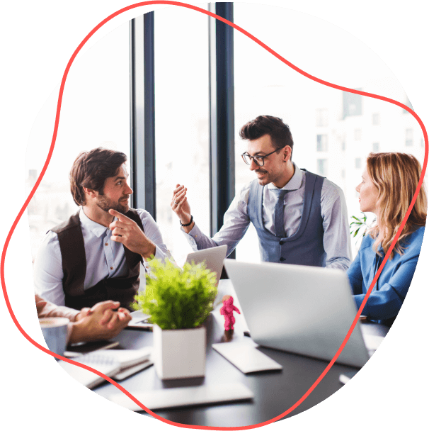 Skupinka zamestnávateľov sa zapája do živej diskusie pri stole, s otvorenými notebookmi, zaliatymi jemnou žiarou slnečného svetla prúdiaceho cez neďaleké okno.